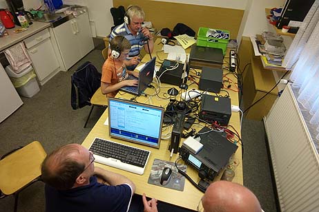 Blick in den Funkraum mit allerhand Funkgeräten, Verstärkern, Netzteilen und Laptops für die Logbuchführung der geführten Funkverbindungen und die digitale Textübertragung auf dem Funkwege.
